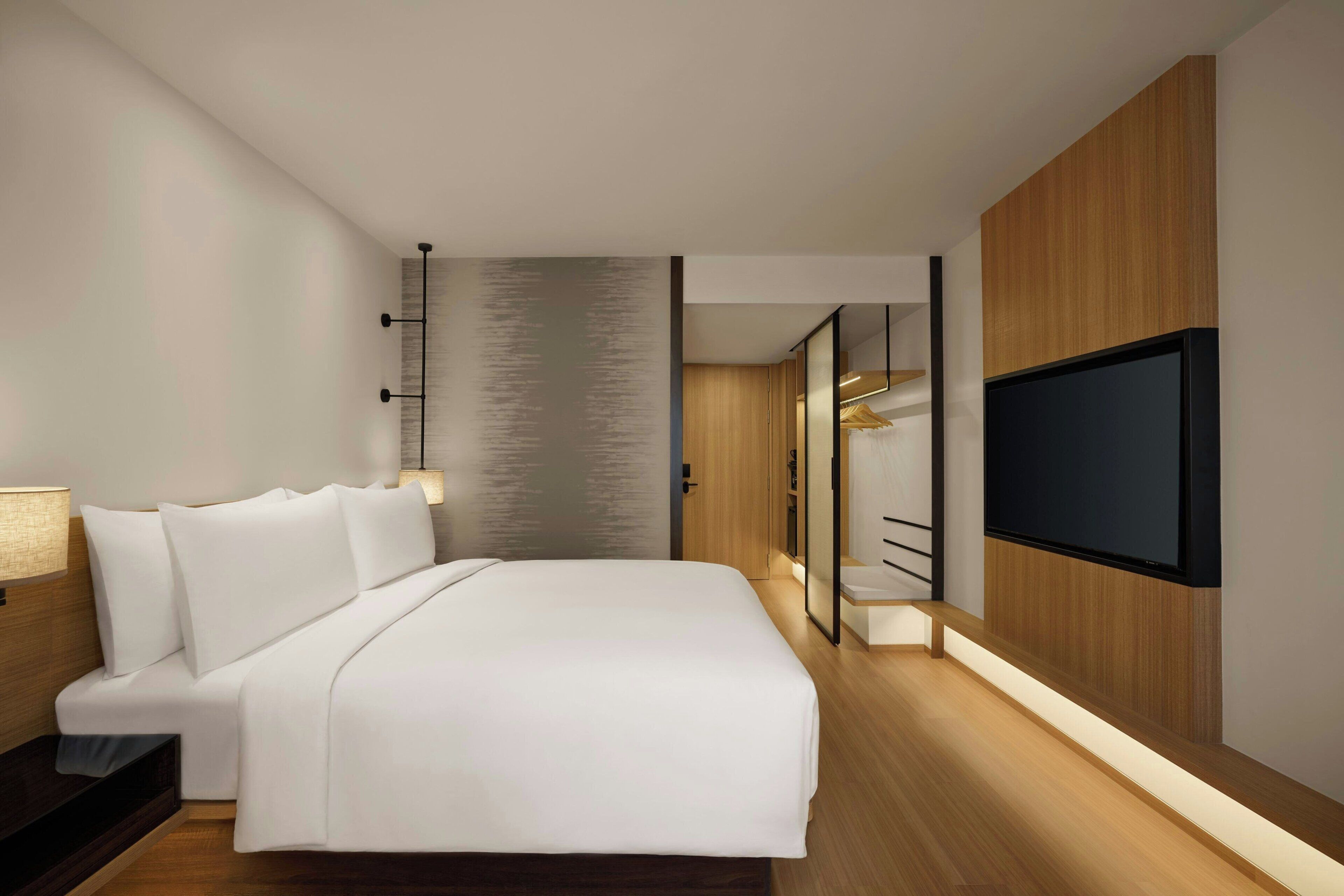 A modern hotel room with a large bed, a TV mounted on the wall, and a wooden floor.