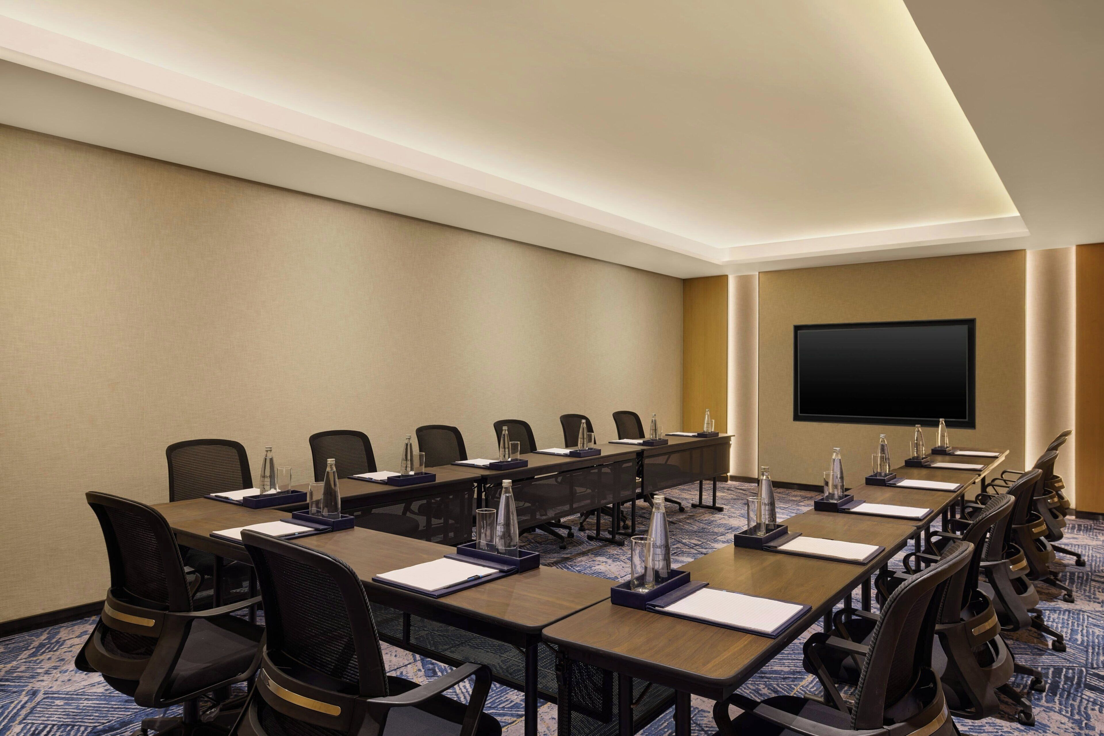 A conference room with a long table, multiple chairs, water bottles, and a flat-screen TV on the wall.