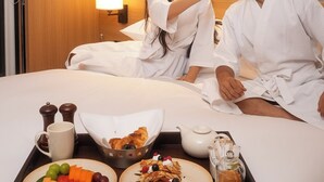 Una habitación de hotel con cama, una bandeja con alimentos para el desayuno y una mesita de noche con lámpara.