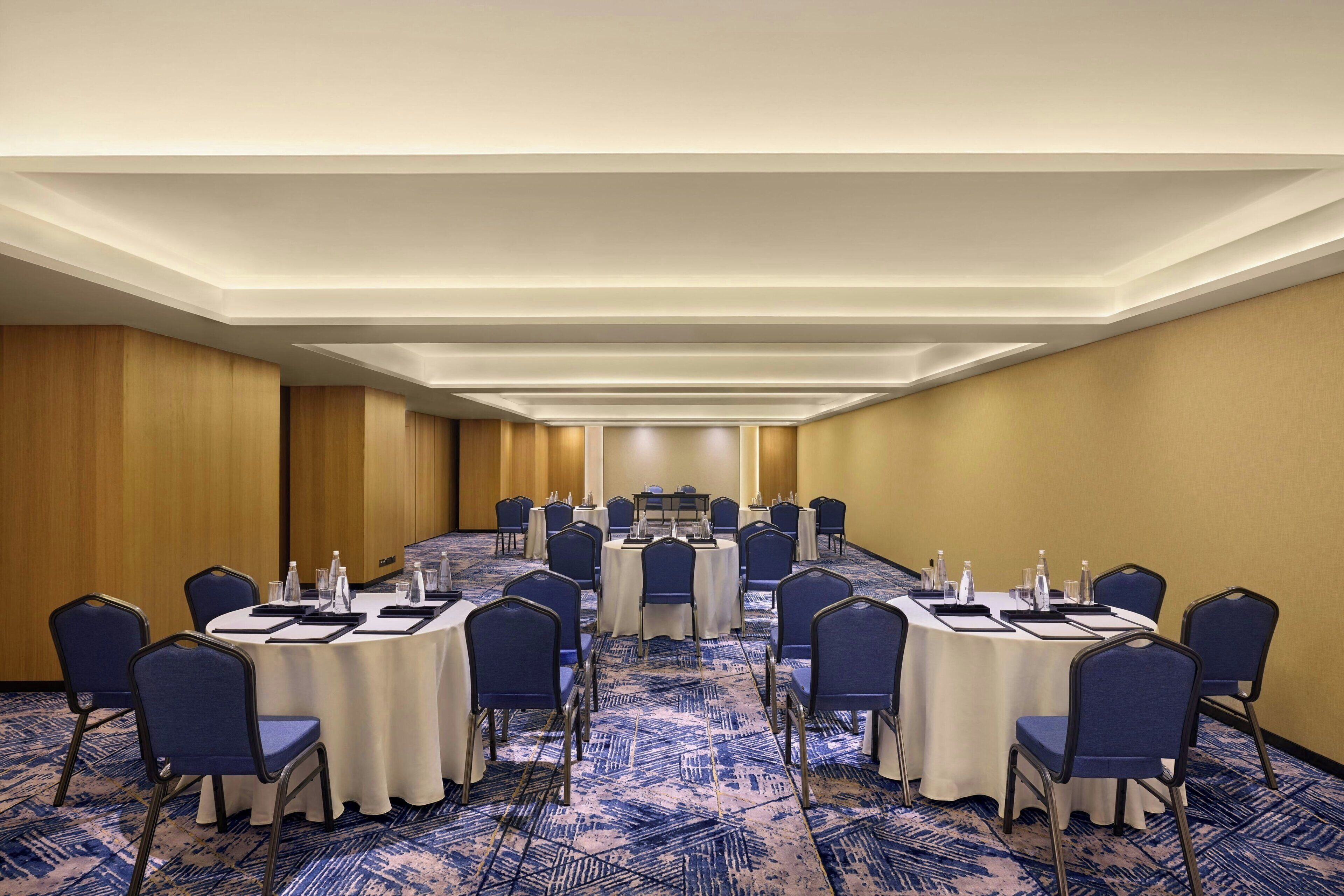 A conference room with round tables and chairs, a carpeted floor, and a wooden panel wall.