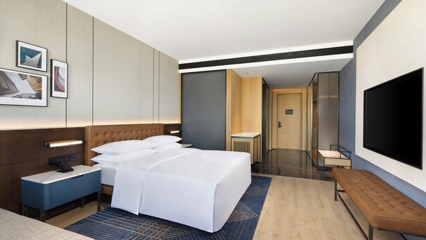 A modern hotel room with a large bed, bedside tables, a flat-screen TV, and a bathroom visible in the background. - Four Points By Sheraton Leshan (Leshan)