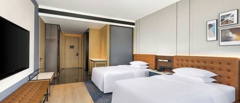 A hotel room with two beds, a TV, a desk, and a bathroom visible through an open door.