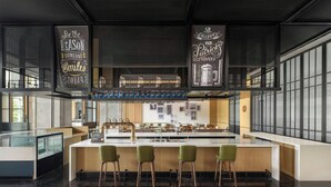 Un espace bar moderne doté d’un îlot central, de tabourets de bar et d’une enseigne suspendue sur laquelle on peut lire : « Soyez la raison pour laquelle quelqu’un sourira aujourd’hui. »