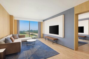 A modern hotel room with a large window, a flat-screen TV, a sofa, a bench, and a small table. - Four Points By Sheraton Leshan (Leshan)