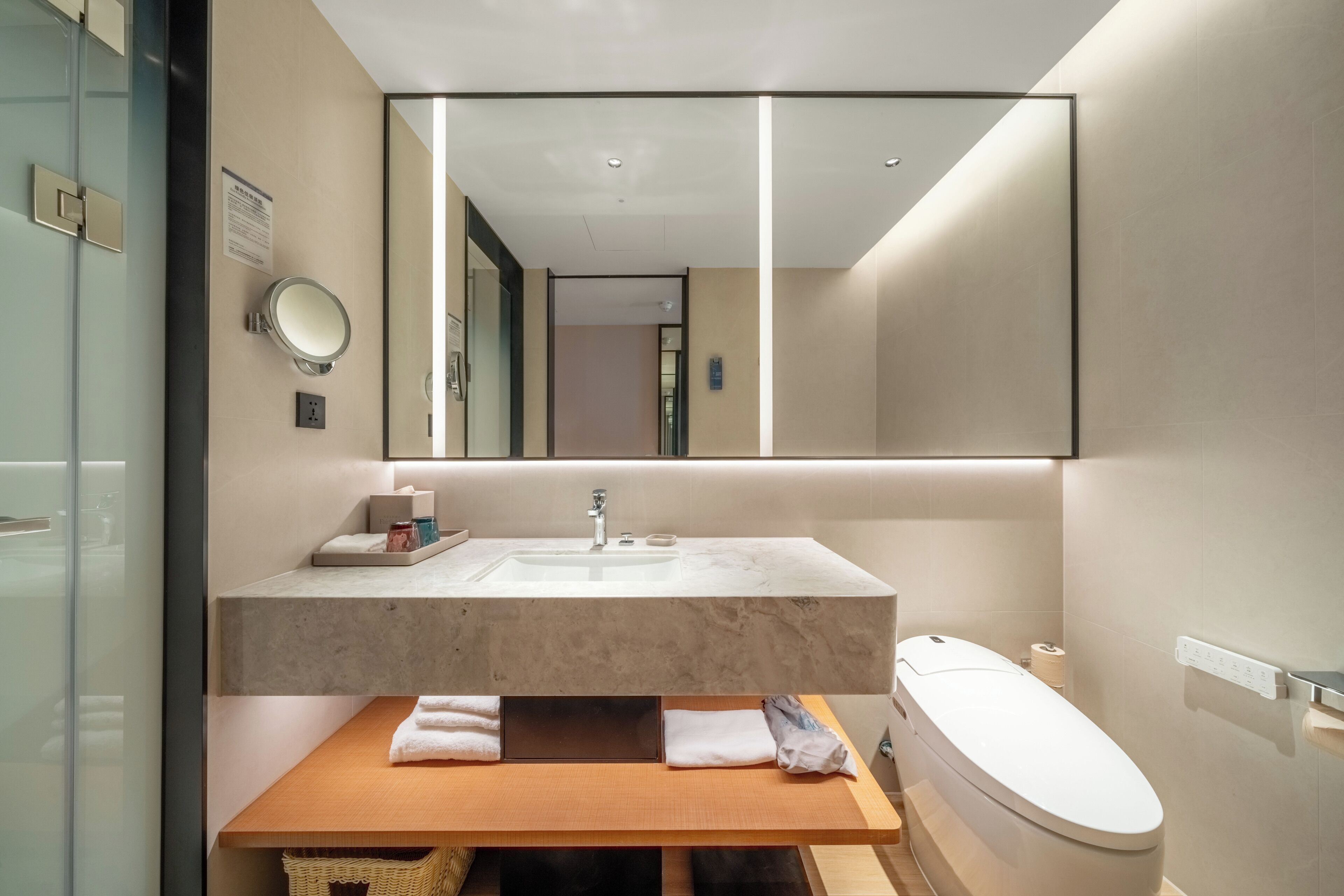 Un baño moderno con lavamanos de mármol, un espejo grande y un inodoro.