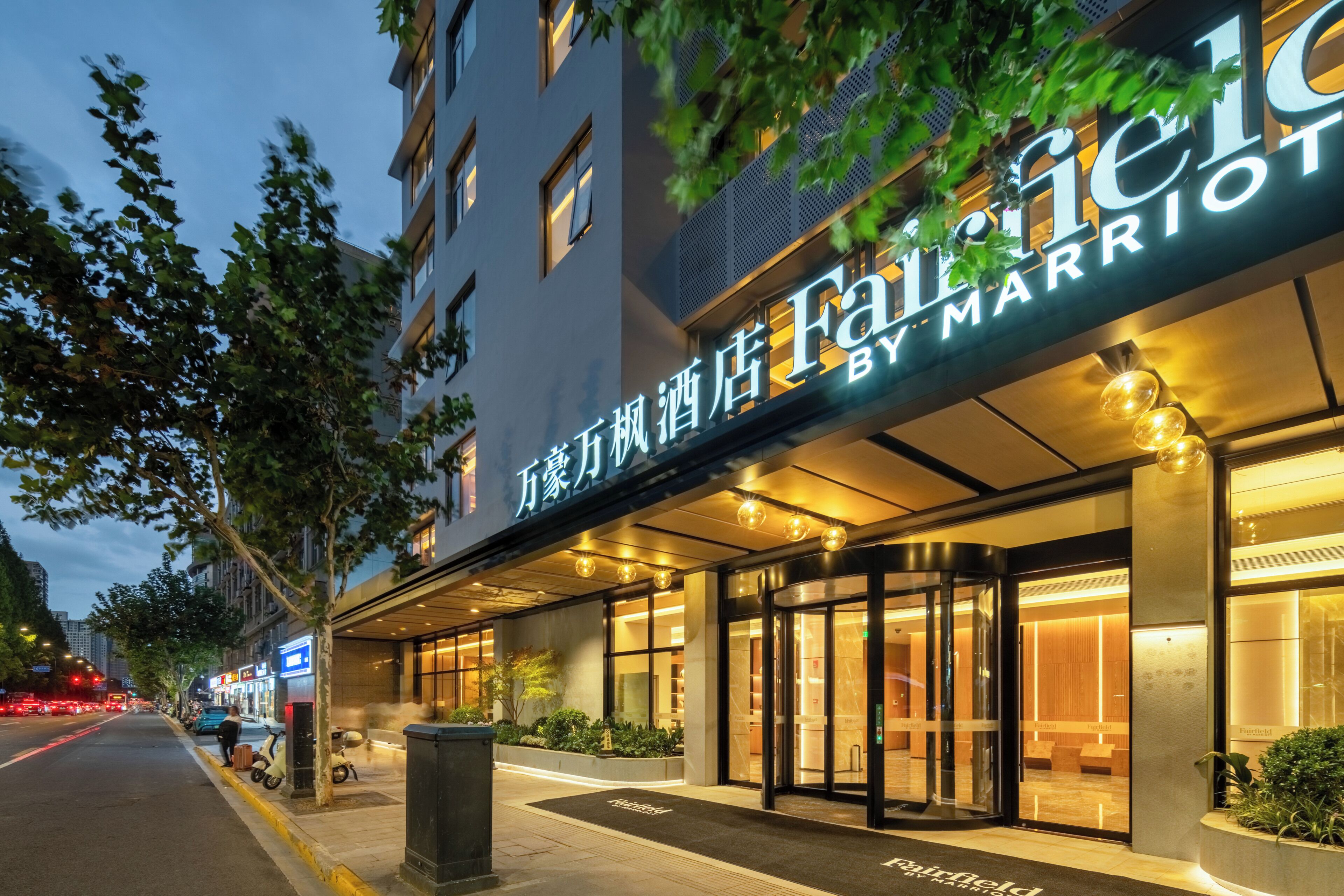 A hotel entrance with a marquee sign, glass doors, and a well-lit facade.