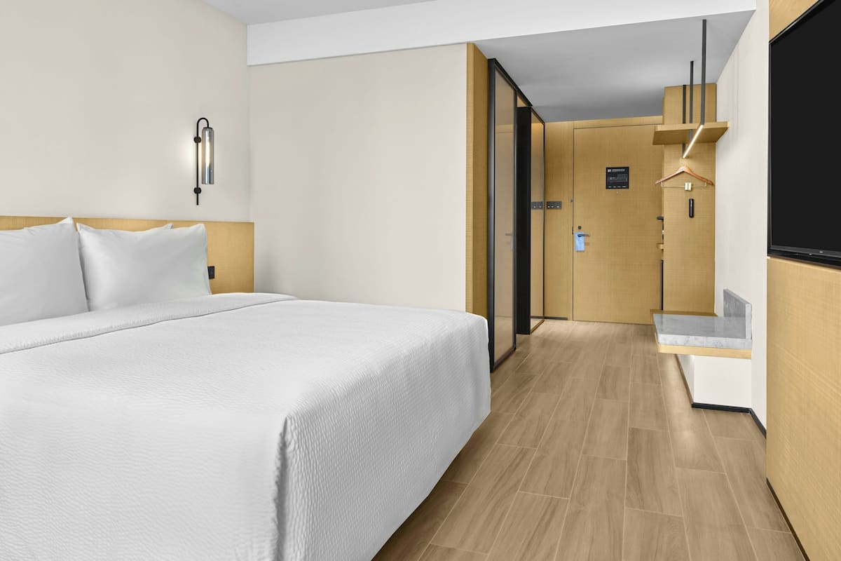 Ein modernes Hotelzimmer mit einem großen Bett, Holzboden, einer Wandleuchte und einer kleinen Sitzecke mit einer Theke.