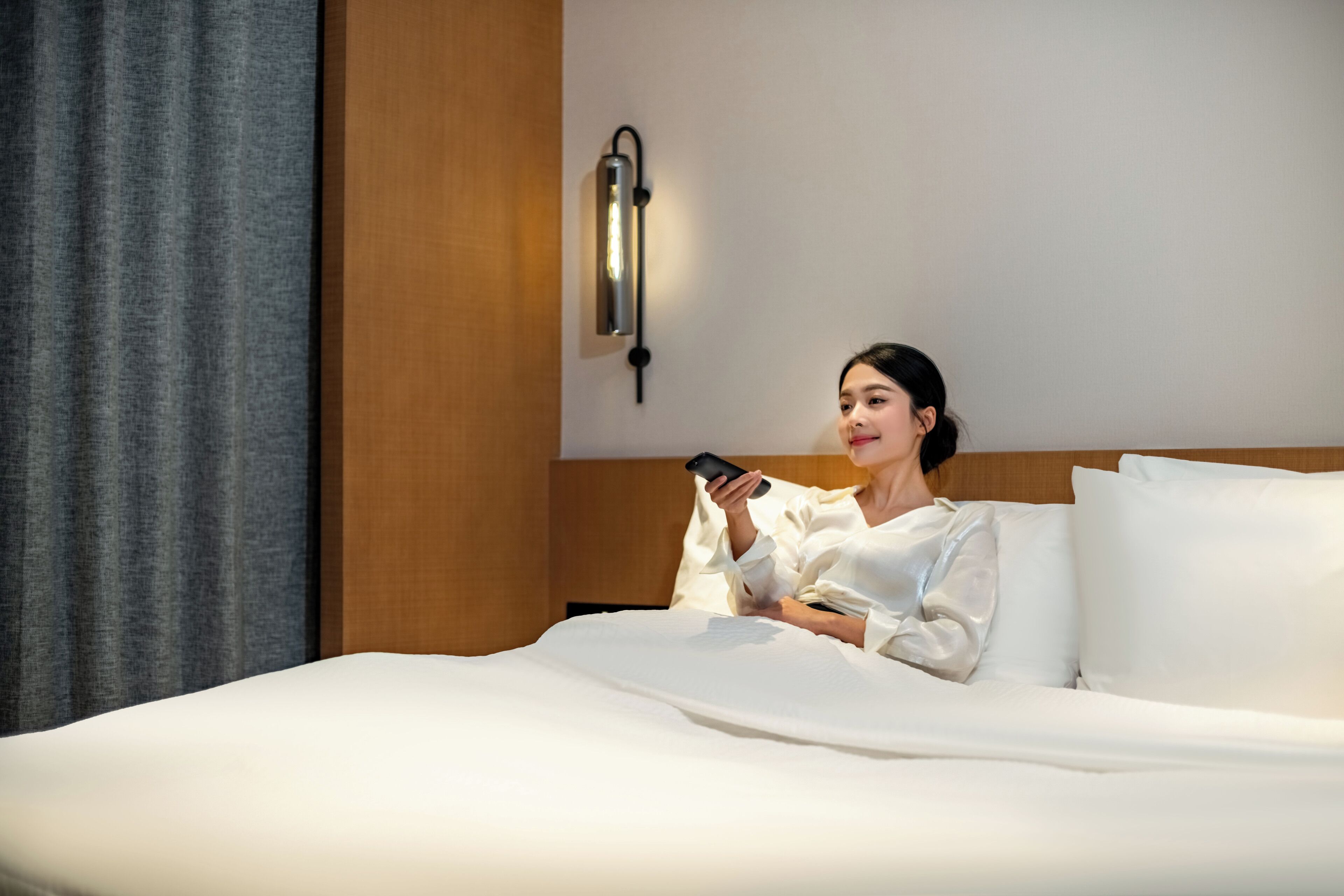 Une personne allongée sur un lit dans une chambre d’hôtel, tenant un téléphone intelligent.