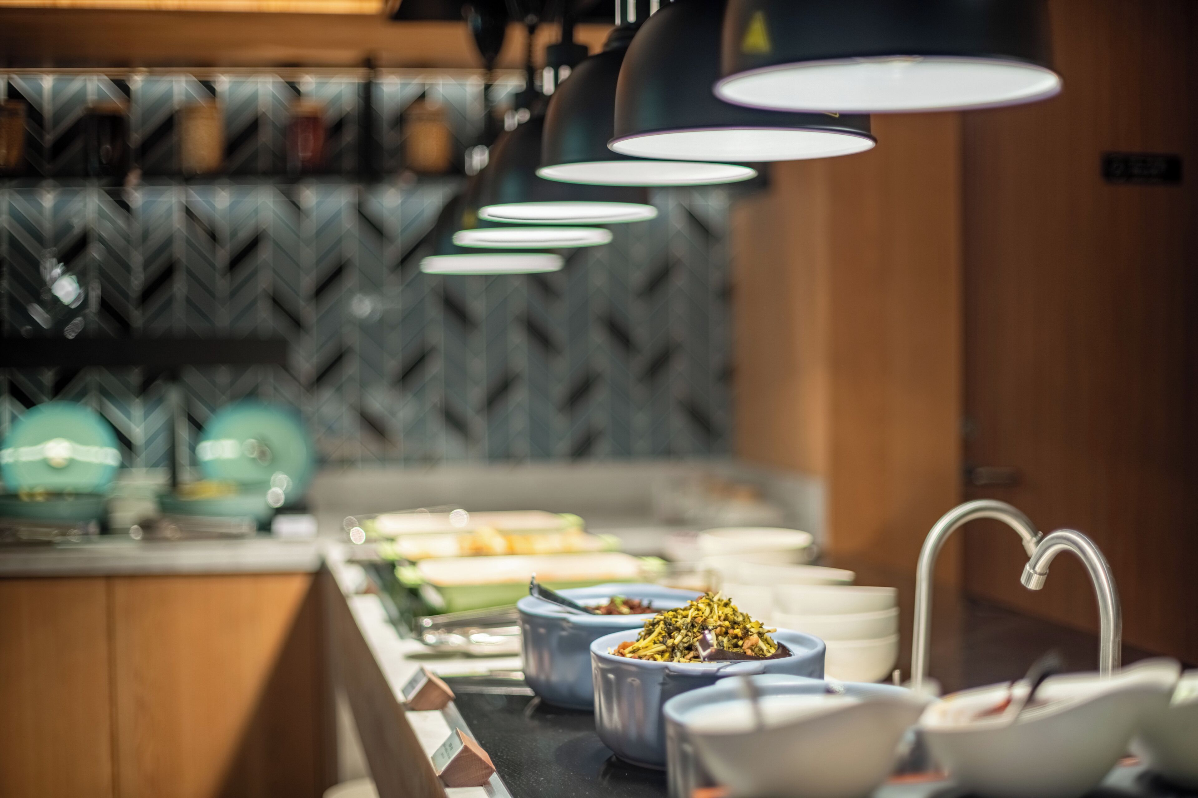 Een buffetopstelling met diverse gerechten en kommen, een moderne keuken met een patroonbelegd spatwand en hanglampen.