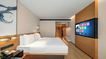 A modern hotel room with a bed, a flat-screen TV, a desk with a phone, and a wall-mounted artwork.