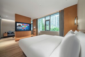 Ein modernes Hotelzimmer mit einem großen Bett, einem an der Wand befestigten Fernseher, einem Fenster mit Blick auf Gebäude und einer kleinen Sitzecke mit Sofa und Beistelltisch.