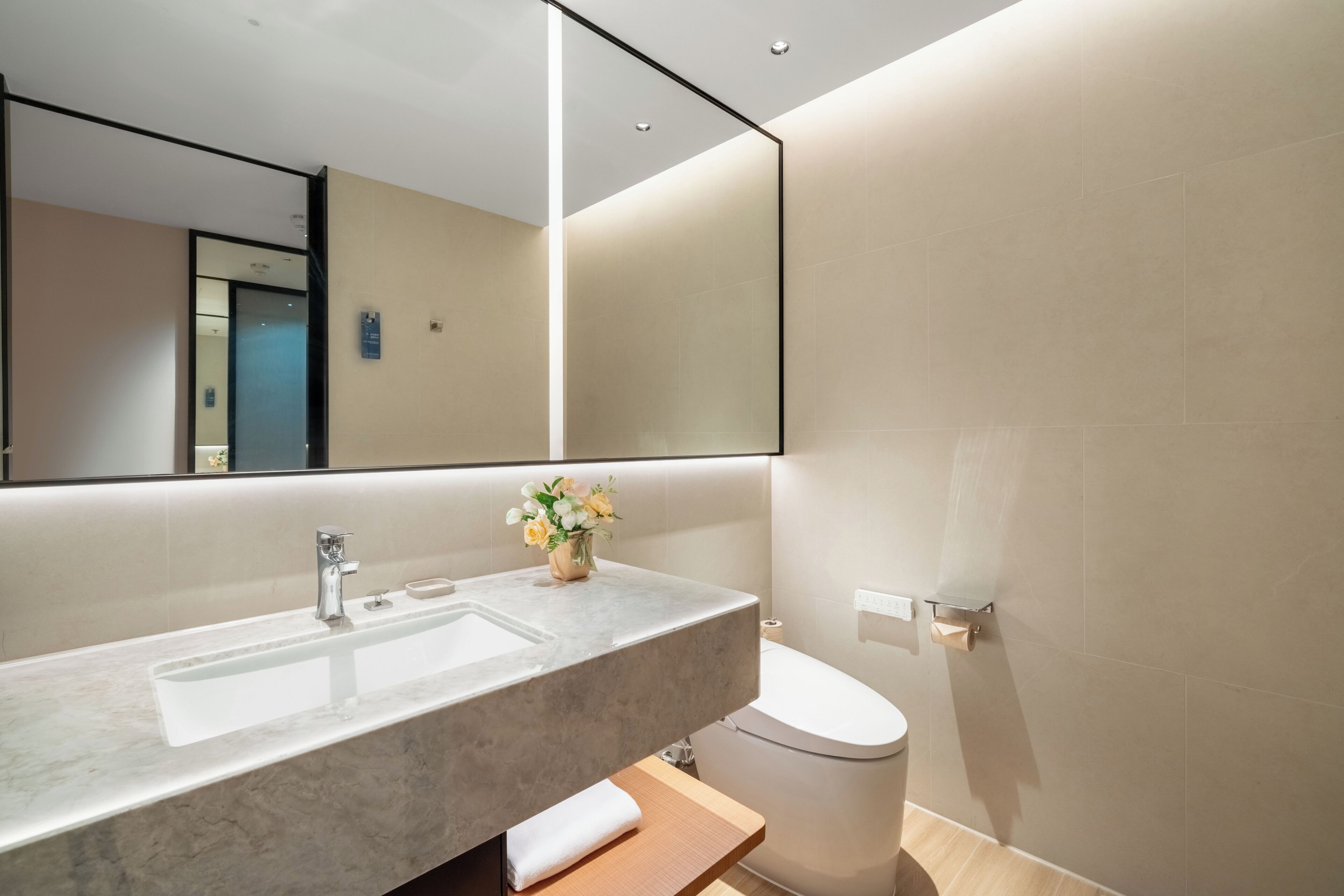 Un baño moderno con lavamanos de mármol, inodoro y un espejo grande.