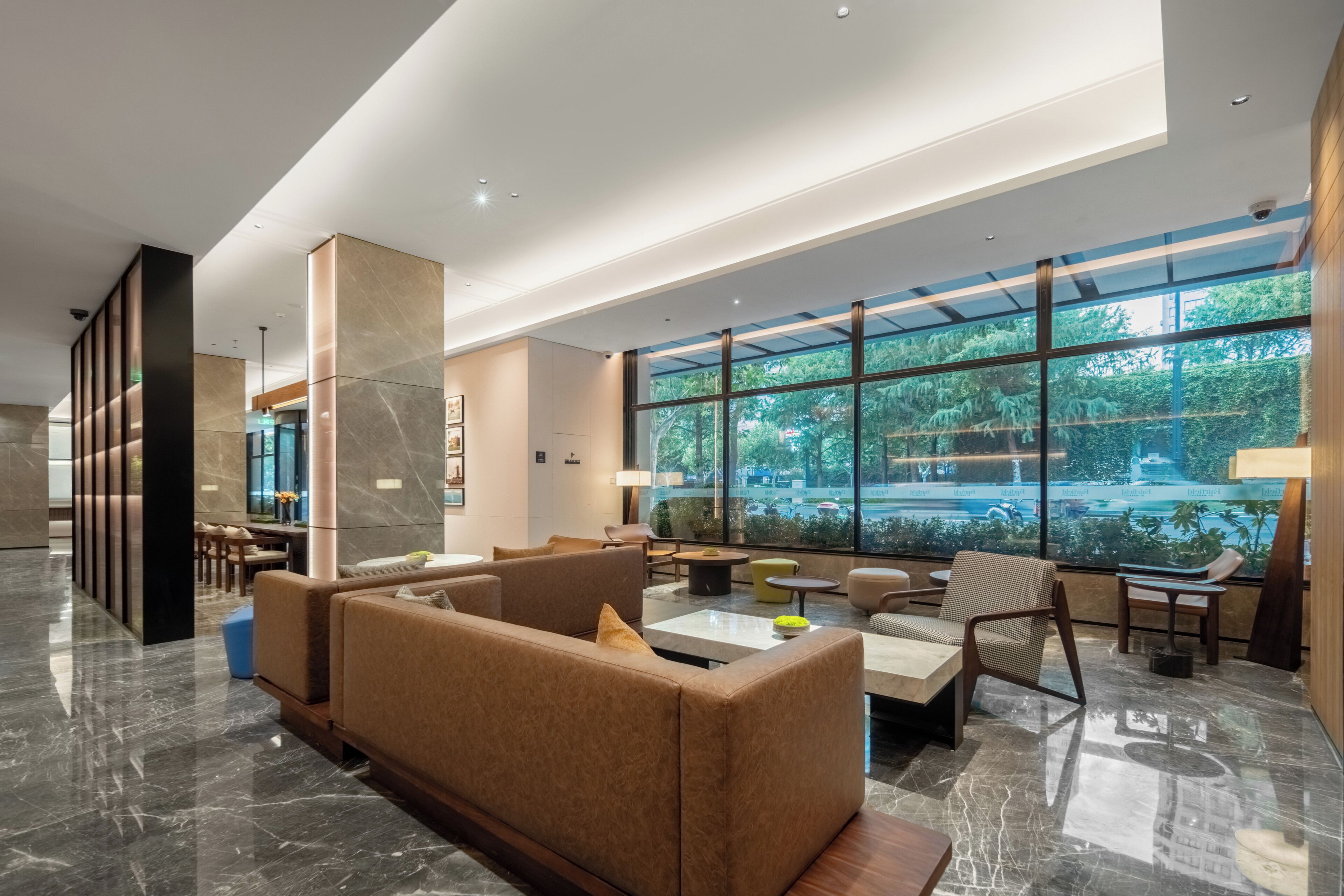 A spacious lobby with a modern design, featuring a large seating area, a reception desk, and a view of a lush garden through expansive windows.