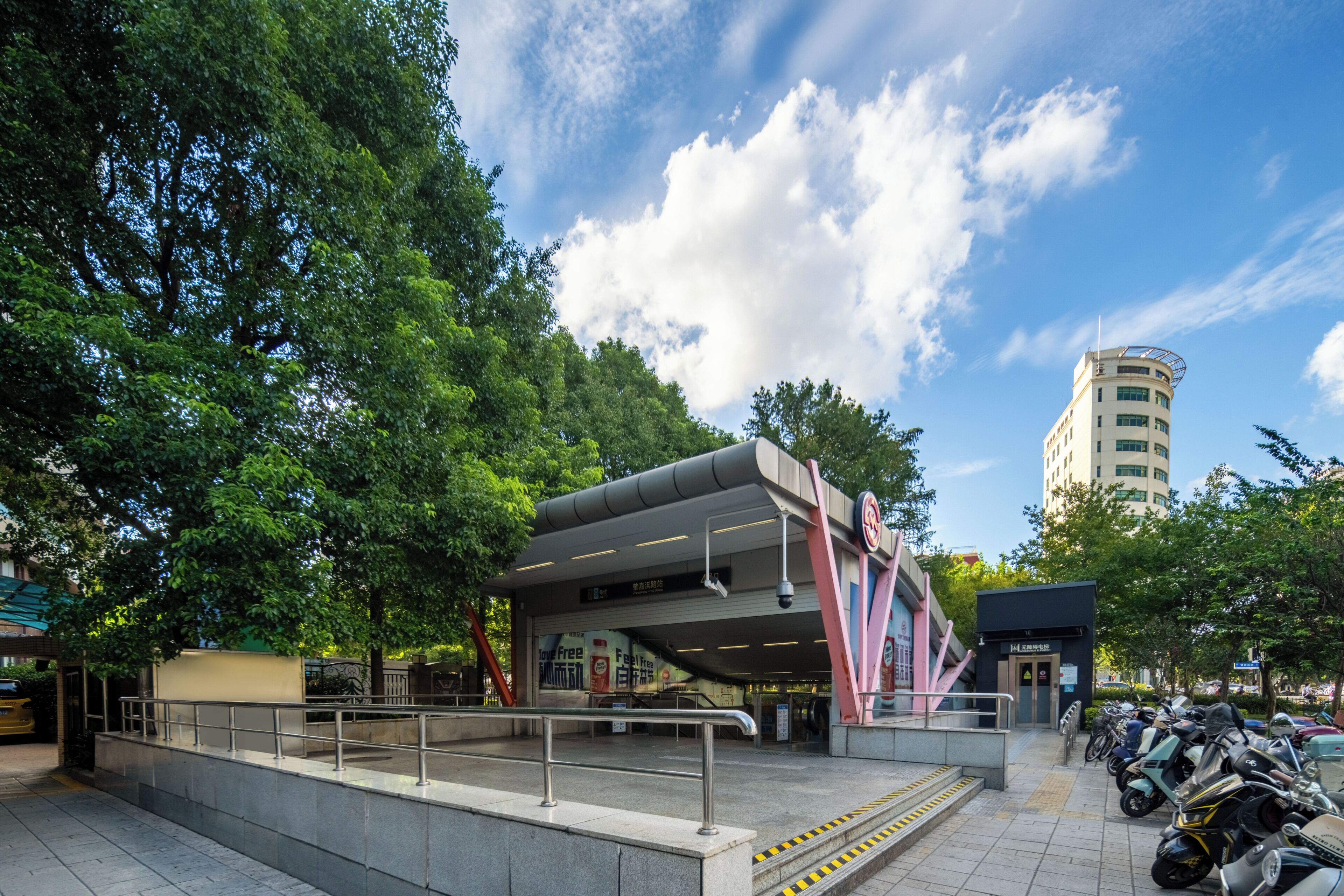 A modern building with a covered entrance, a staircase leading up to it, and a parking area with motorcycles.