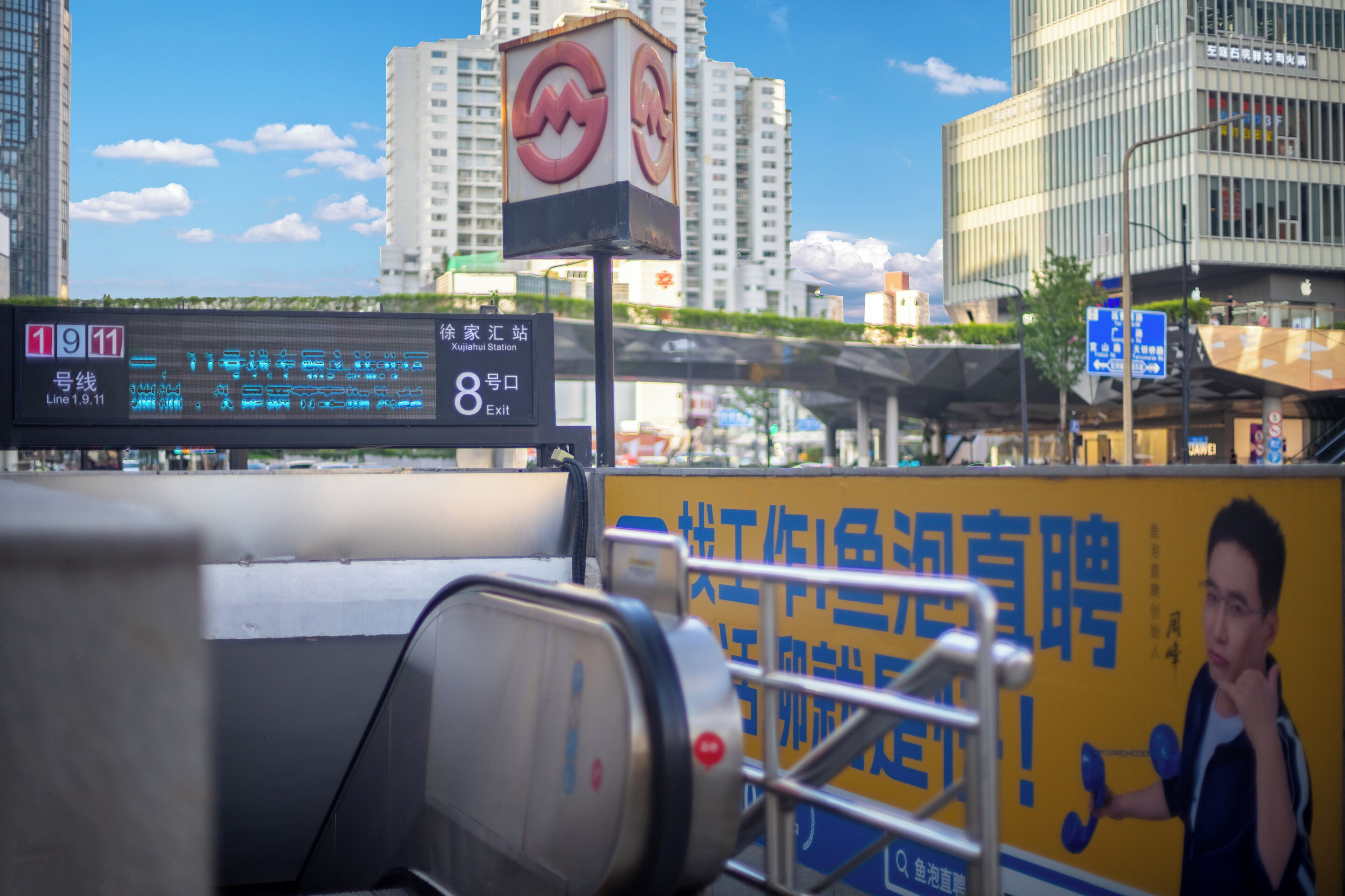 Um ônibus com tela digital exibindo a rota e o número da parada, cercado por edifícios urbanos e um céu claro.