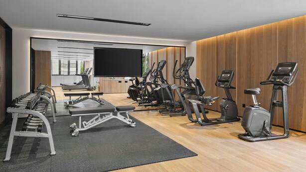 Un gimnasio moderno con diversos equipos de ejercicio, un televisor y un amplio ventanal.