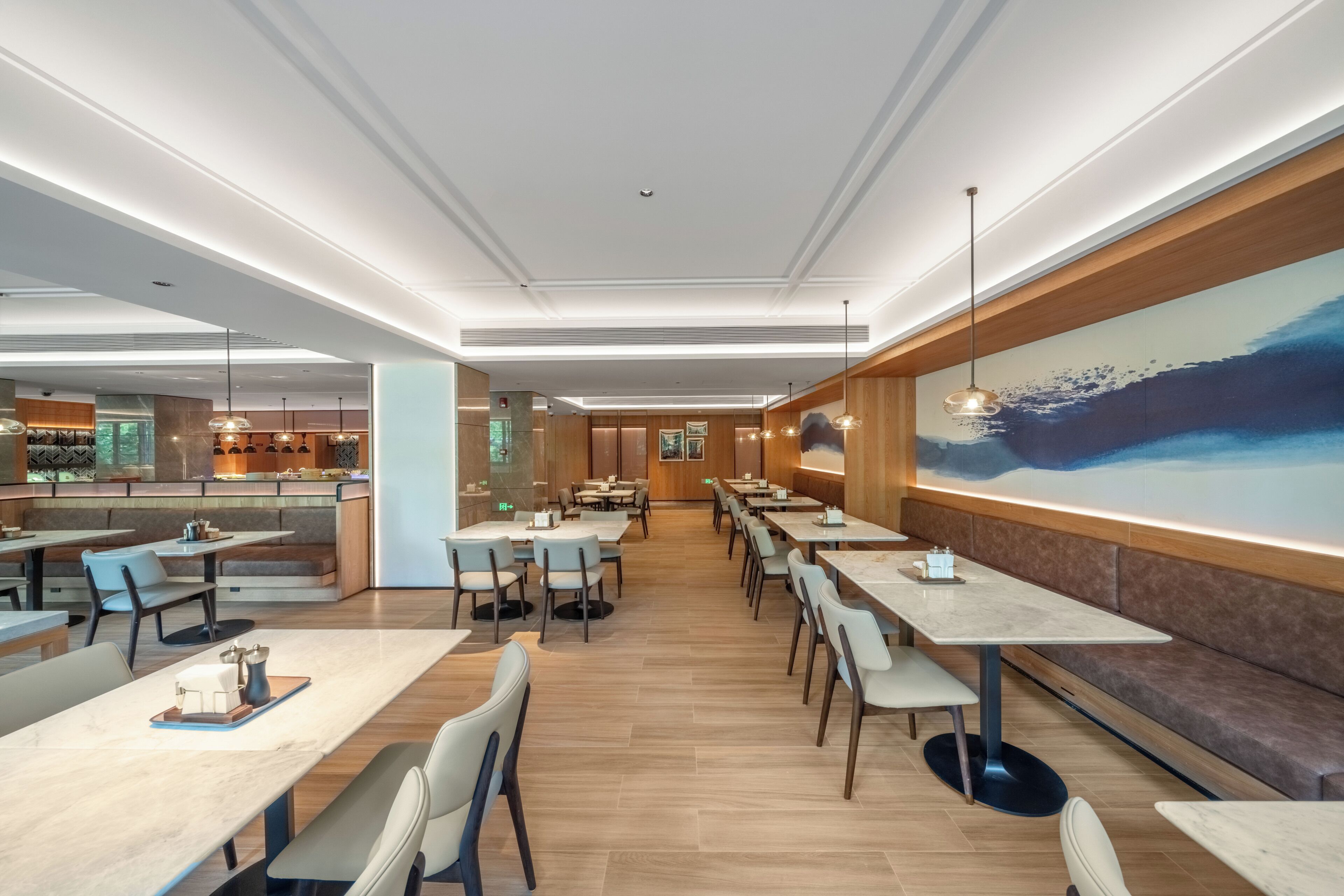 A modern restaurant with multiple dining areas, a bar, and a large mural on the wall.