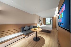 Una habitación de hotel moderna con sofá, una mesita redonda con un jarrón, una cama y un televisor grande mostrando iconos de aplicaciones.
