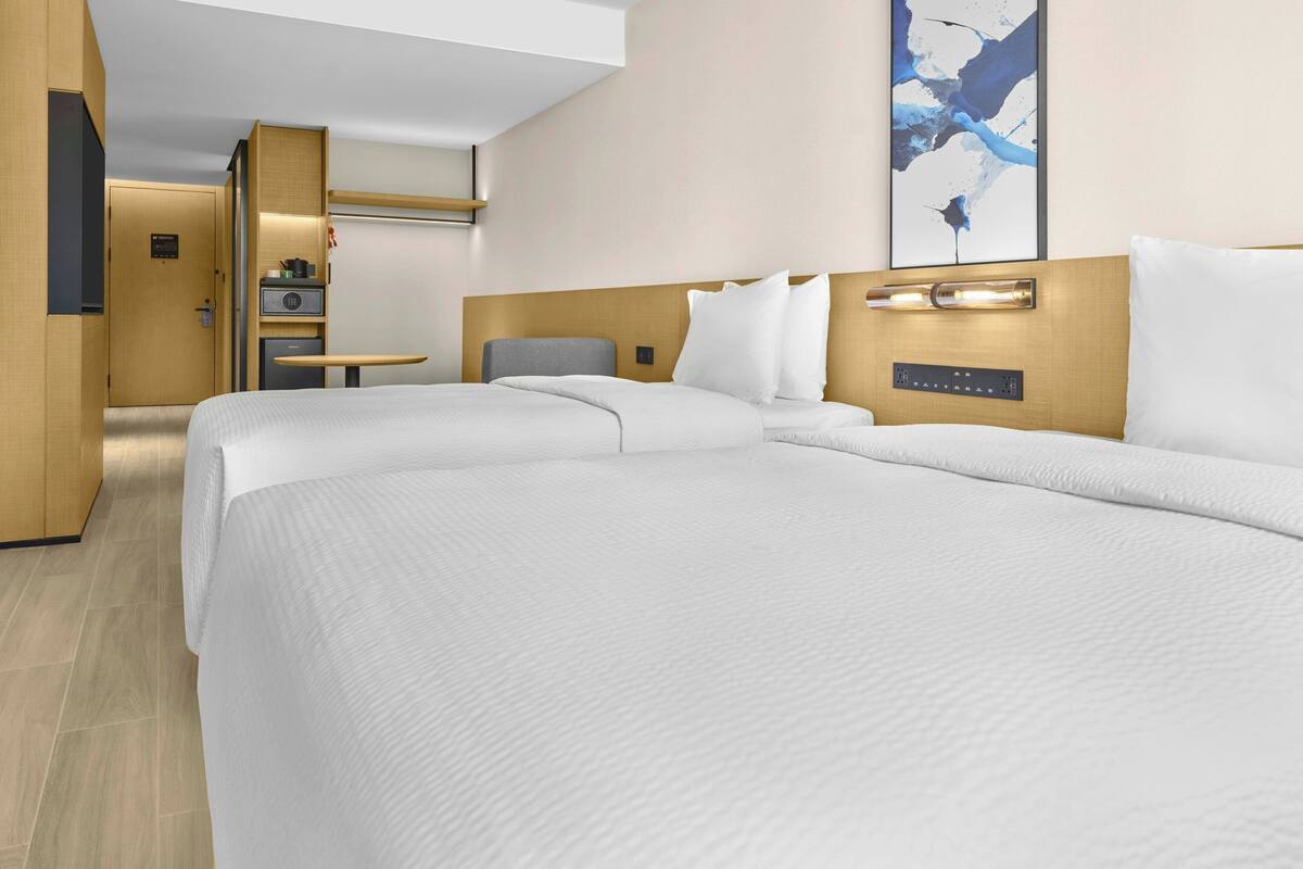 Ein Hotelzimmer mit zwei Betten, einem Schreibtisch, einem Stuhl und einer kleinen Küchenzeile.