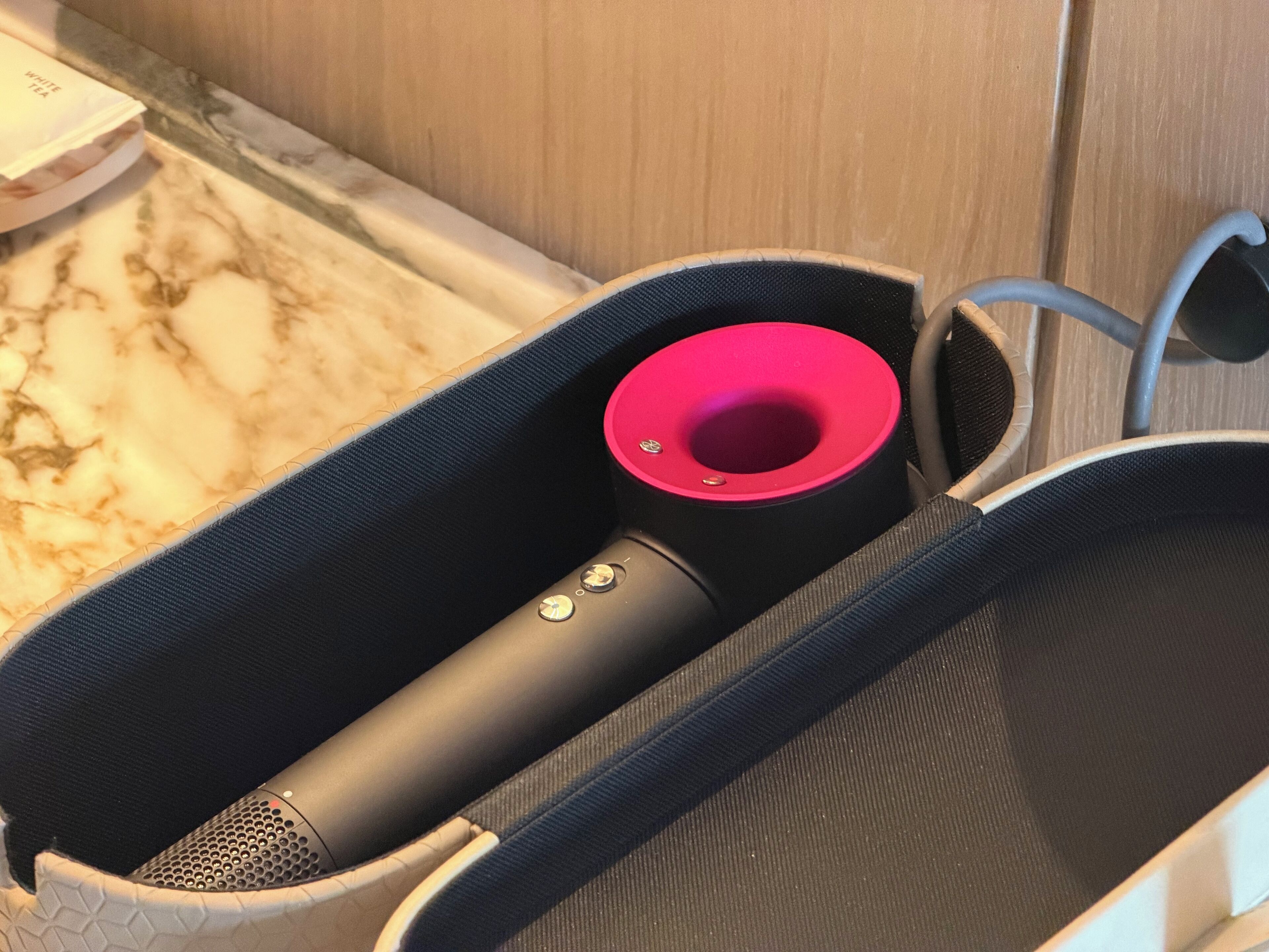 A black portable speaker in a black mesh bag with a pink accent, placed on a marble countertop.
