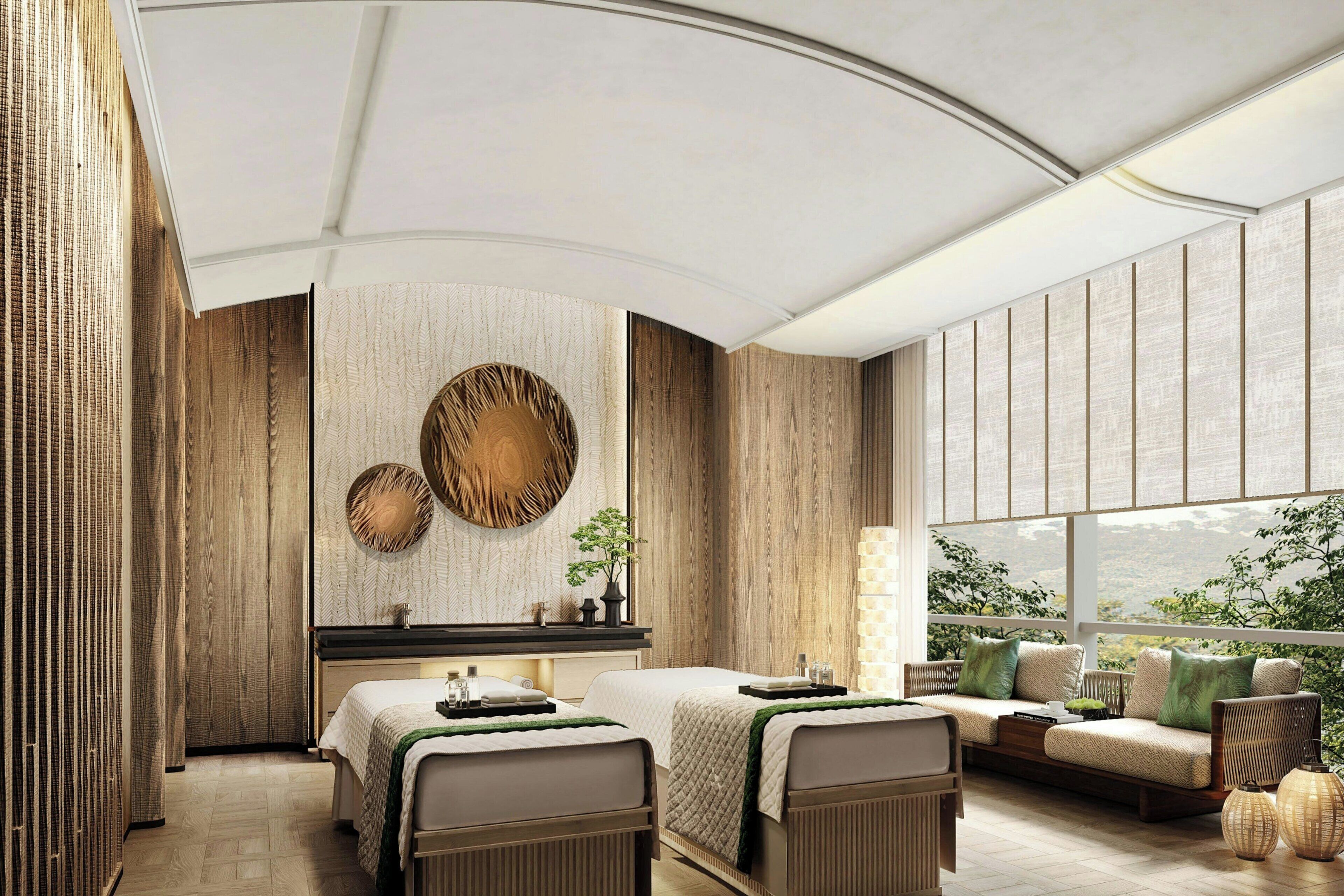 A modern hotel room with a large bed, a sofa, and a view of greenery.