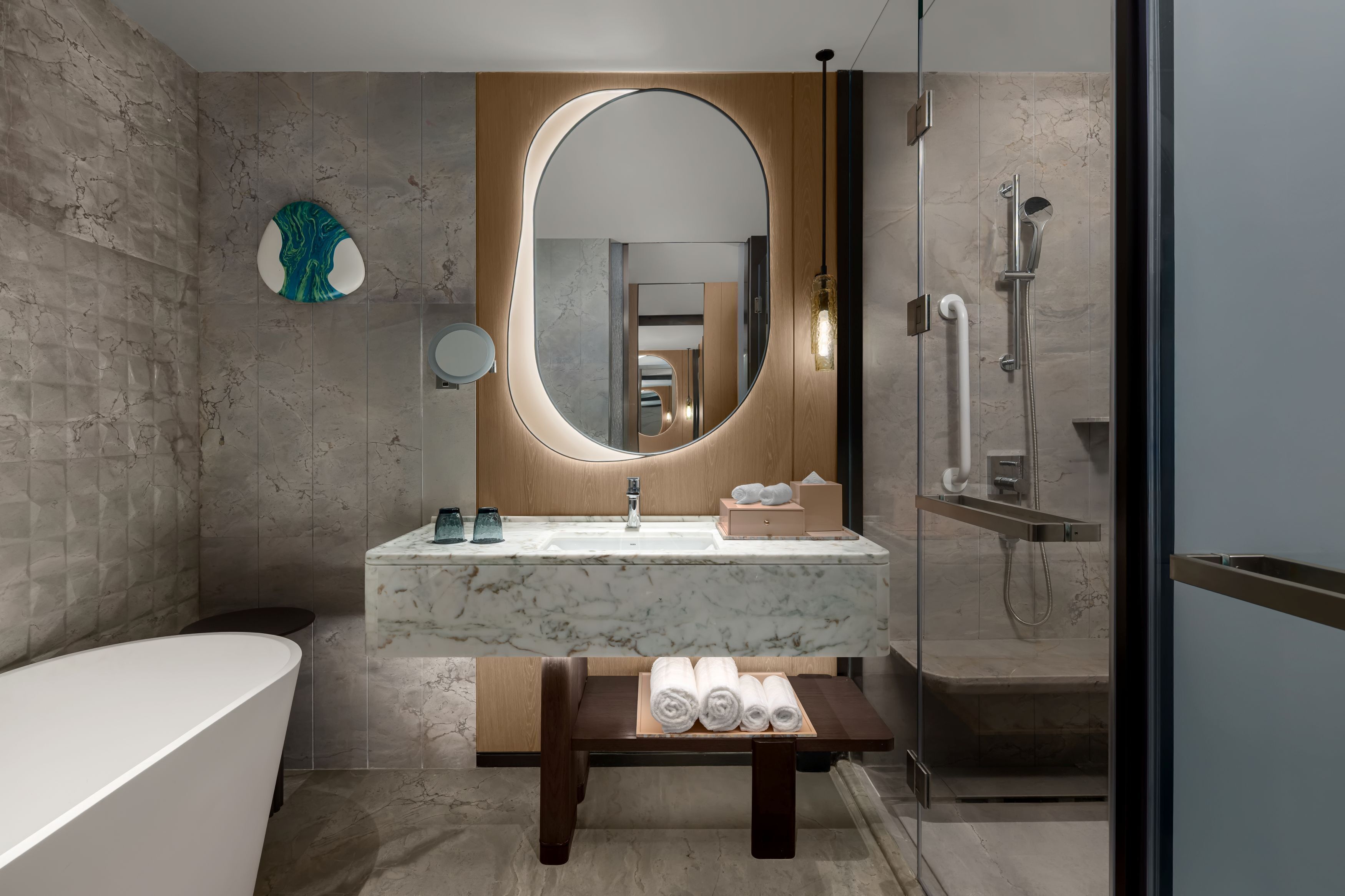 Un baño moderno con lavamanos de mármol, un espejo ovalado grande, una bañera y una ducha.