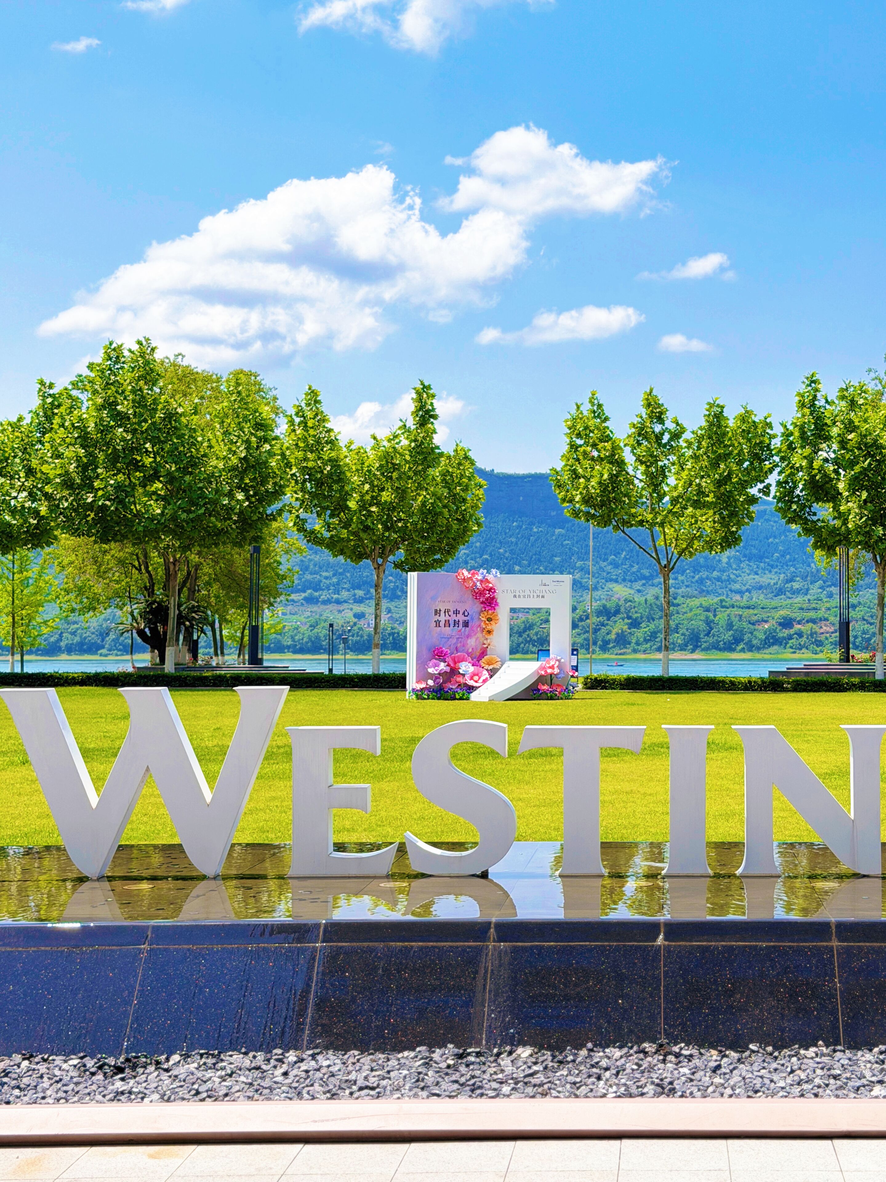 Une grande enseigne extérieure avec le mot « WESTIN » en lettres majuscules, entourée d’un élément décoratif aquatique et d’arbres.