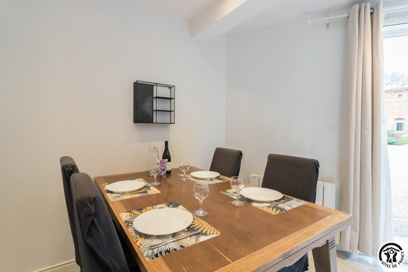 A dining table set for four with a bottle of wine, glasses, and plates.