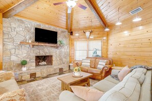 Una sala de estar acogedora con chimenea de piedra, techo de madera, sofá de cuero y televisor de pantalla plana montado en la pared.