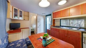A compact kitchenette with wooden cabinets, a sink, and a window with blinds. - Mobilhouse in campsite Seafront (Lotzorai)