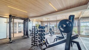 A modern gym with various exercise equipment, large windows, and a wooden ceiling. - Beachfront Condo Studios With Pool in Bessa Beach - Gses (João Pessoa)