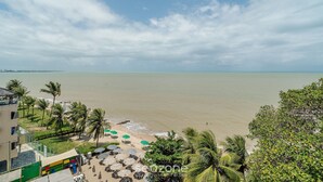 A beach view with palm trees, umbrellas, and a building with a green facade. - Beachfront Condo Studios With Pool in Bessa Beach - Gses (João Pessoa)