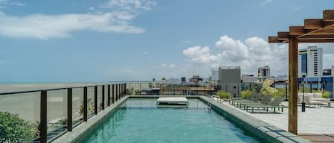 A rooftop pool with a view of the beach and city skyline.