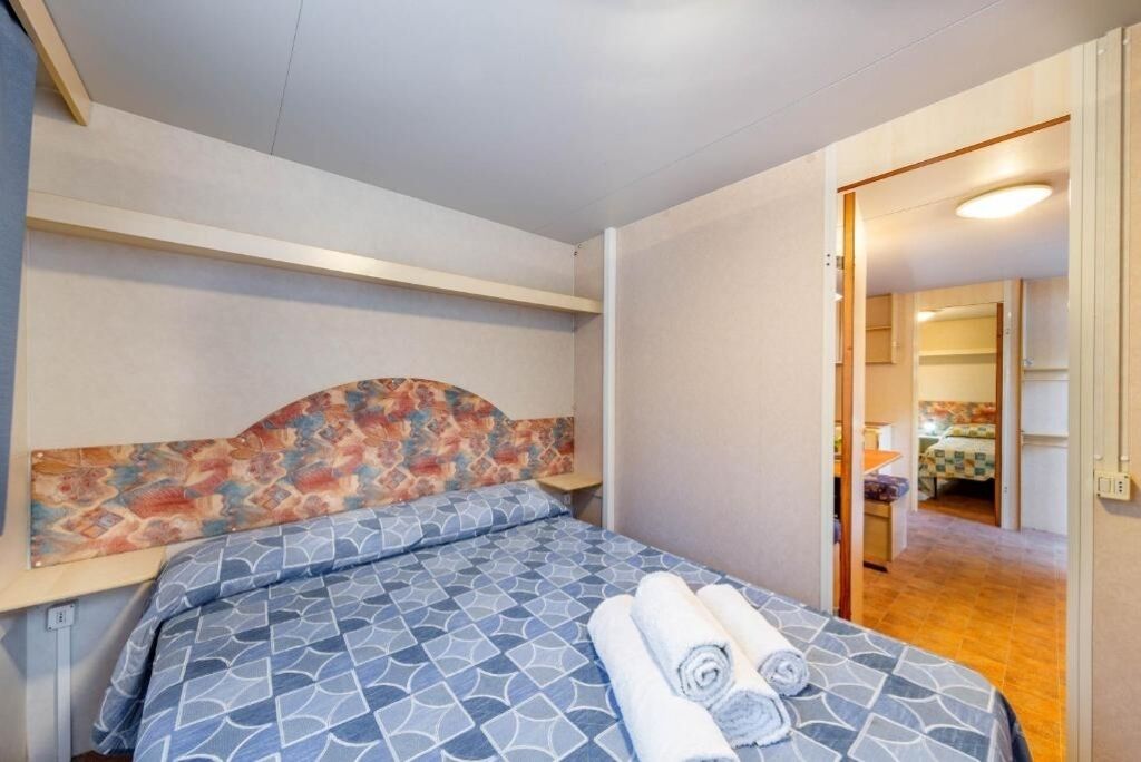 Ett hotellrum med en säng, en sänggavel med ett färgstarkt mönster och en väl bäddad säng med hoprullade handdukar.
