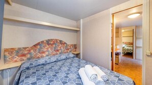 A hotel room with a bed, a headboard with a colorful pattern, and a neatly made bed with rolled towels.
