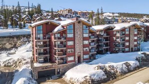A multi-story hotel with balconies, a stone facade, and a view of a snowy mountain landscape. - Raven's Reach in Happy Valley - Private Hot Tub & Shared Pool (Beaverdell)