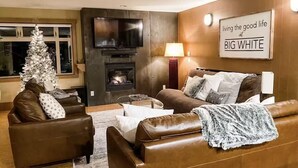 A living room with a fireplace, leather sofas, a Christmas tree, and a sign reading "living the good life at BIG WHITE". - Raven's Reach in Happy Valley - Private Hot Tub & Shared Pool (Beaverdell)