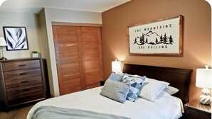 A bedroom with a bed, wooden wardrobe, and a framed quote on the wall.