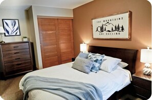 A bedroom with a bed, wooden wardrobe, and a framed quote on the wall.