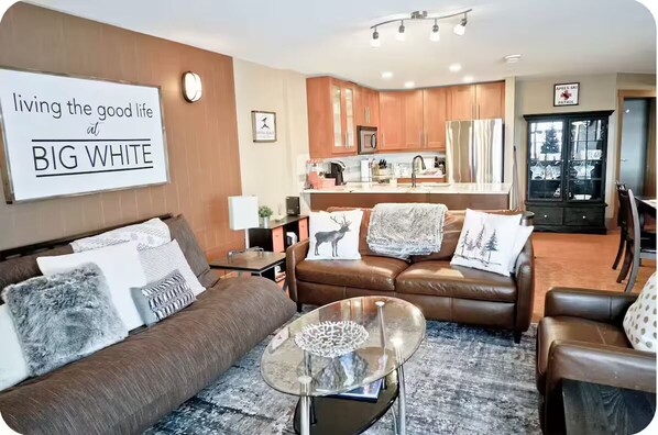 Un salon avec un canapé en cuir marron, une table basse en verre et une pancarte sur laquelle on peut lire : « Profitez de la belle vie à BIG WHITE. »