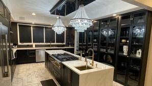 A modern kitchen with a central island, black cabinetry, and a marble floor. - Beach Park Estate: Chef's Kitchen, Nature, Fitness Room, Naval Base, Beach, Lake (Beach Park)
