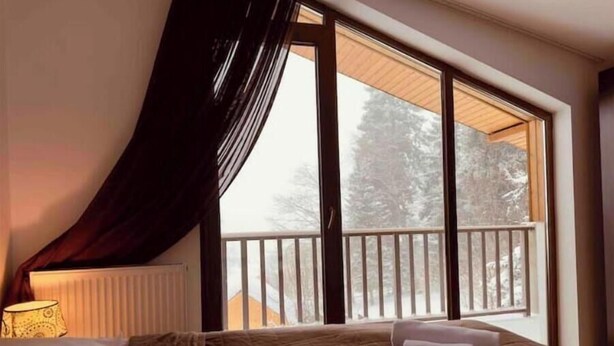 Une chambre avec une grande fenêtre, un lit recouvert d’une courtepointe et une table de chevet avec une lampe.