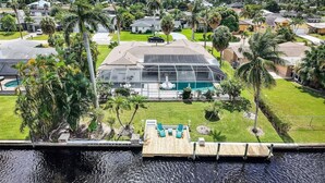 A residential property with a large glass house, a swimming pool, and a wooden deck. - Waterfront Home with Heated Pool, Air Hockey, Beach Gear & MORE! (Cape Coral)