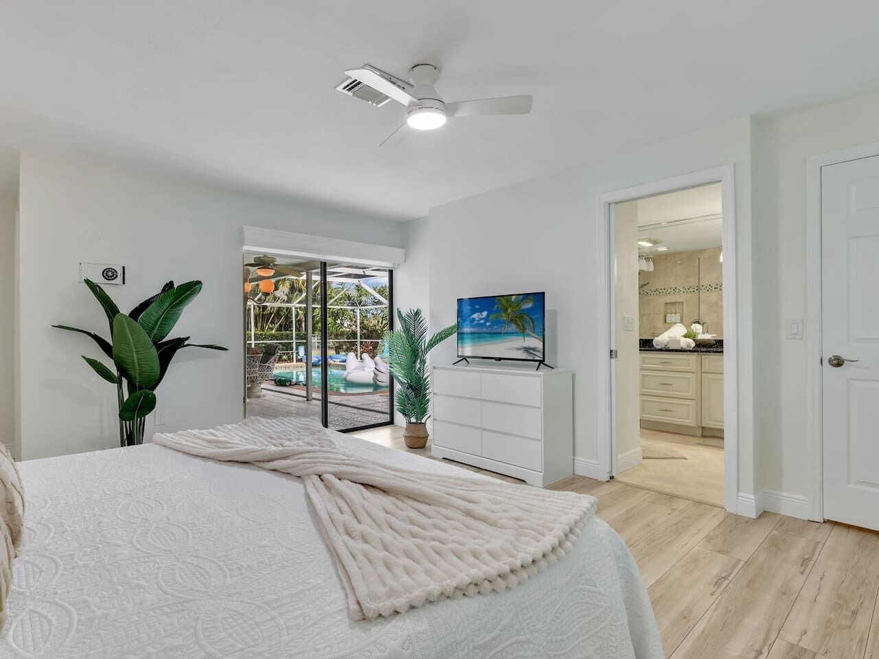A bedroom with a bed, a ceiling fan, a TV, and a view of a pool and outdoor area.