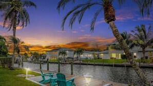 A waterfront property with a dock, outdoor seating, and a view of the water and sunset. - Waterfront Home with Heated Pool, Air Hockey, Beach Gear & MORE! (Cape Coral)