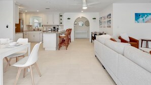 A modern living room with a sofa, dining table, and chairs. There is a kitchen area with cabinets and a countertop. - Waterfront Home with Heated Pool, Air Hockey, Beach Gear & MORE! (Cape Coral)