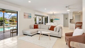 A spacious living room with a large sectional sofa, a coffee table, and a view of a swimming pool. - Waterfront Home with Heated Pool, Air Hockey, Beach Gear & MORE! (Cape Coral)