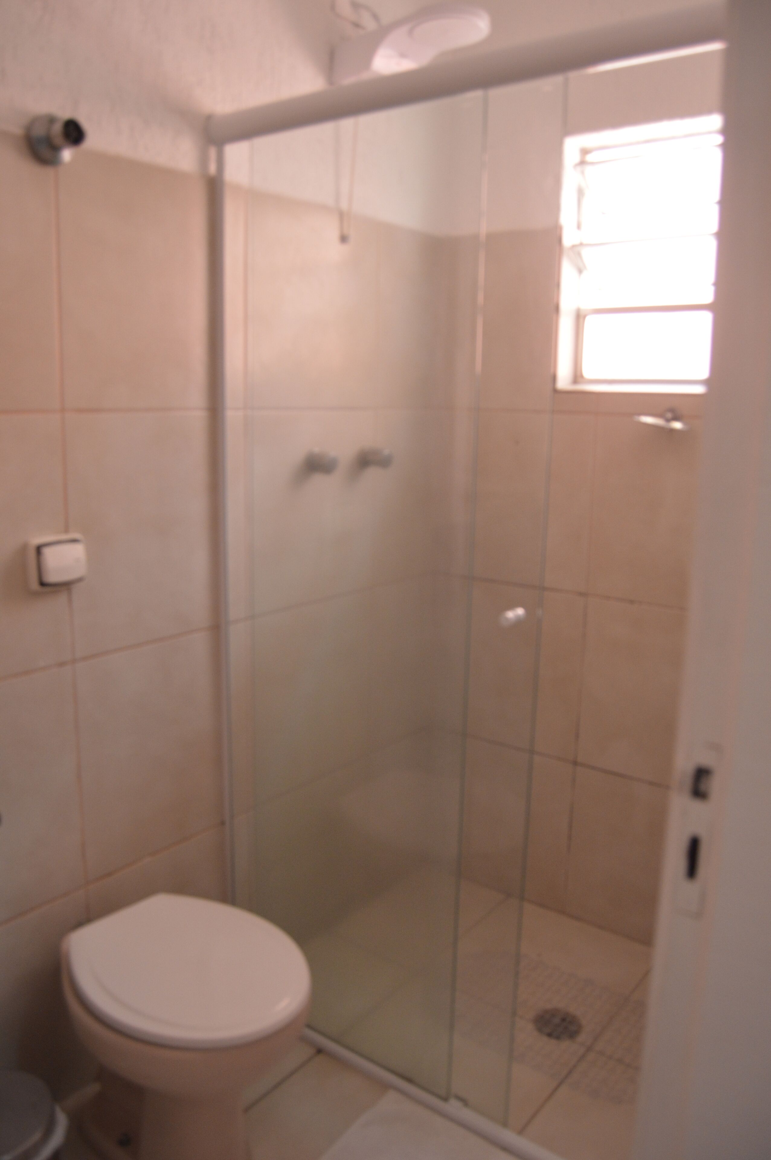 Un baño con inodoro, ducha con cerramiento de vidrio y ventana.