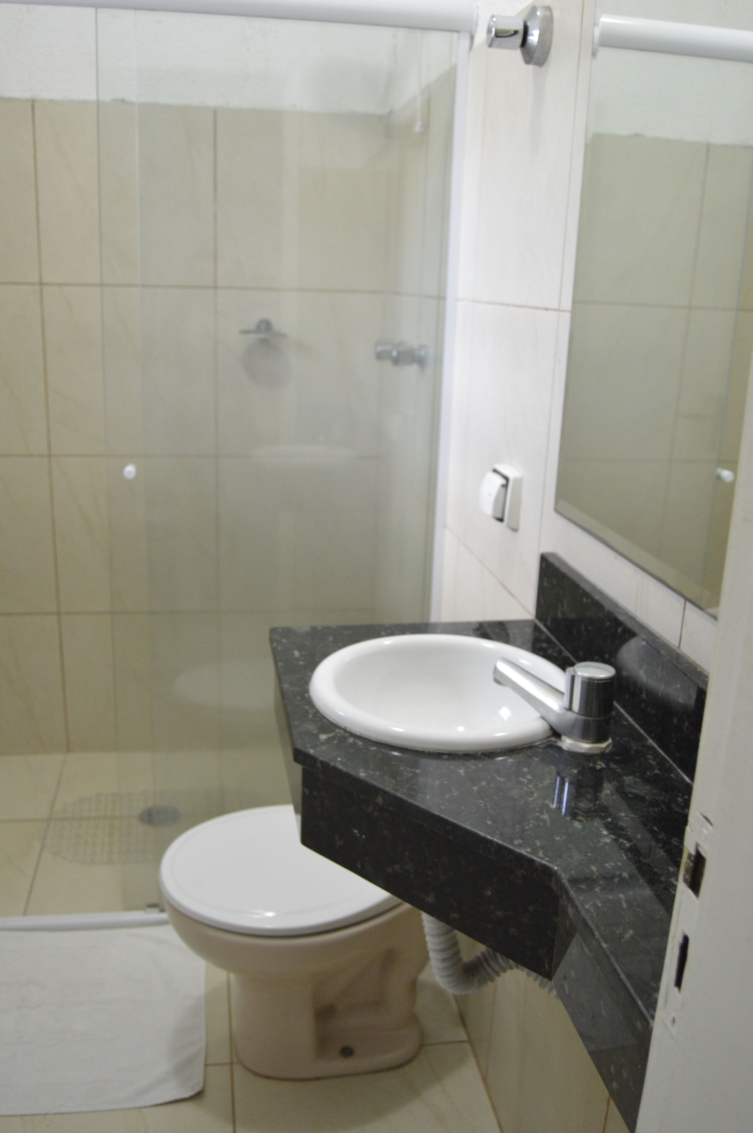 Een badkamer met een wit toilet, een wastafel met een zwart aanrechtblad en een douchecabine van glas.