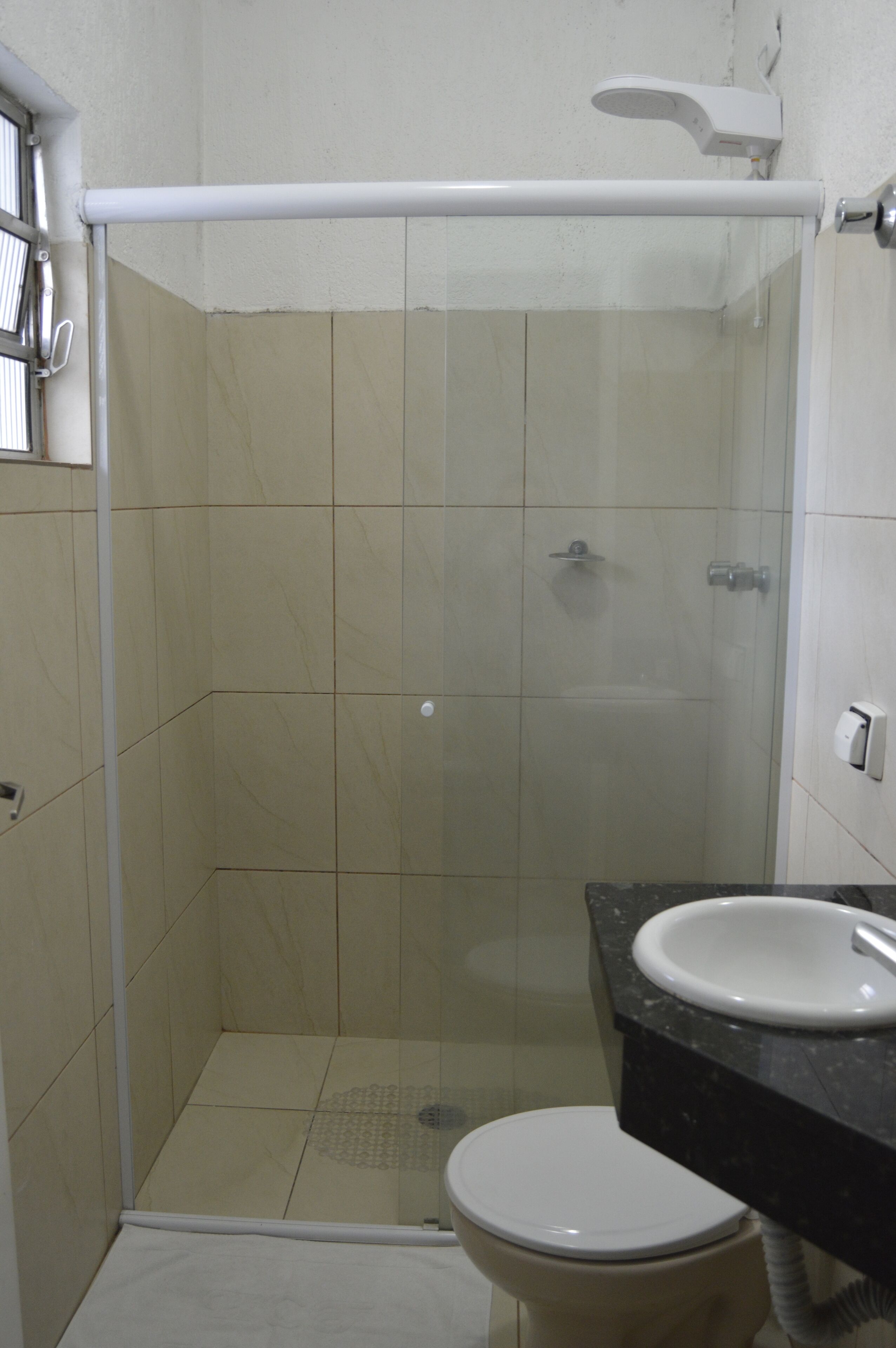 A bathroom with a glass-enclosed shower, a toilet, and a sink with a black countertop.